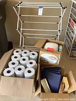 View including foldable clothes drying rack, Diaper Genie box with refill, paper towels, and other household items in boxes.