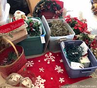 Photo showing the assortment of holiday items on a red snowflake rug including a Santa figurine, wreaths, poinsettias, and plastic bins.