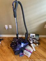 Full view of Kenmore canister vacuum with hose and wand, Kenmore vacuum bags, Black & Decker handheld vac and a small Black & Decker vacuum on the floor.