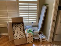 Wide shot showing laundry baskets, ironing board, stools, and paper products