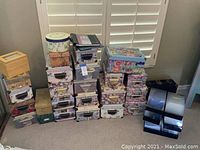 Multiple floral and patterned photo storage boxes stacked on carpet in front of window shutters.