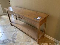 Wood sofa table positioned against a wall, showing the turned legs, carved front applique, and lower shelf.