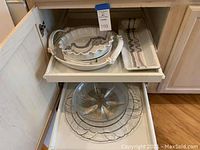 Stoneware platters and glass serving platters arranged in kitchen cabinet drawers and shelves.