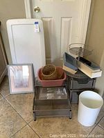 Assorted storage containers and organizational items arranged on floor against door including plastic bins, wicker baskets, metal organizers, and white waste bin.