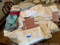 Full assortment of linens displayed on table including placemats, napkins, and tablecloths with visible lace edges and pastel colors
