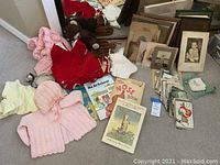 Overall view of vintage baby clothes, assorted children's books, framed photographs, and postcards spread on floor.