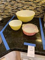Three vintage Pyrex bowls on black countertop: two yellow and white mixing bowls and one pink measuring bowl with clear sides.