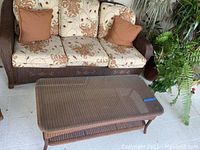 Full view of couch with floral cushions and brown throw pillows along with the wicker coffee table in front.