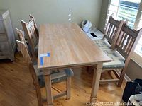 Overall view of wood kitchen table and four wood chairs with fabric seats on a hardwood floor near a window.