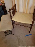 Wood chair with turned spindle arms and padded cream-colored seat showing wear.