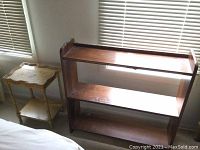 Wooden bookshelf and side table placed near window, showing wood finish and condition.