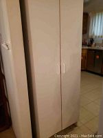 Full view of white storage cabinet with two doors standing in a kitchen area.