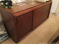 Full view of medium brown wooden credenza with sliding doors on a carpeted floor, showing general condition and size.