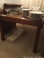 Photo of wooden dining table with plates and glassware on top, showing the table surface and legs.
