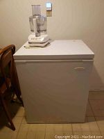 White Frigidaire chest freezer with a food processor placed on top, showing overall size and condition.