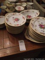 Photo showing stacked large dinner plates, salad plates, cups, and creamers with floral designs and gold rims.