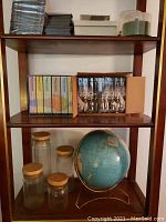Shelf showing Civil War VHS series, Winston S. Churchill books, glass canisters with wooden lids, vintage globe on metal stand.