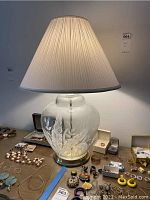 Front view of glass ginger jar lamp with pleated off-white shade, showing etched leaf and floral design around base.