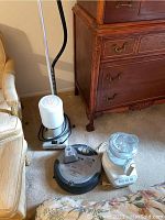 All items visible together: Roomba vacuum, Jiffy garment steamer and KitchenAid food processor on carpeted floor next to furniture.
