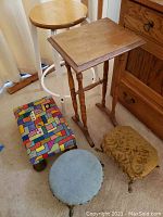 Front view showing the wooden side table, round stool, and three footstools with fabric covers, placed on carpeted floor near wooden dresser.