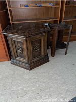 Two wooden side tables, one large octagonal with metal decorative handles, and a smaller rectangular table beside it on a vinyl tiled floor.