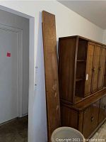 Two long wooden shelves leaning against a wall near wooden furniture. Shelves show scratches and rough marks.