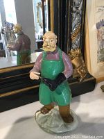 Overall view of the Bohemian art glass shoemaker figurine standing on a surface with a mirror in the background.