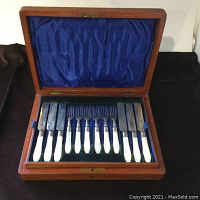 Full view of the open walnut box revealing six forks and six knives with mother of pearl handles arranged in blue satin lining.