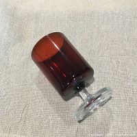 Single burgundy red stemware glass laid on its side showing the solid red bowl with clear stem and foot.