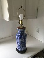Full view of the electrified Chinese vase lamp showing the blue and white porcelain base with hand carved dark wood stand, bare bulb in brass fitting, and wooden ring at the neck.
