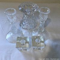 Photo of five crystal candlesticks on white cloth showing large, tall, and cube-shaped holders.
