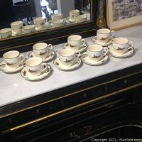 Eight cups and saucers displayed on a marble surface with a large mirror reflecting the set, showing their overall condition and design.