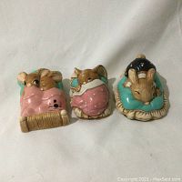 Front view of three Pendelfin bunny figurines in bedtime scenes showing pink and teal bedding and a nightcap detail.