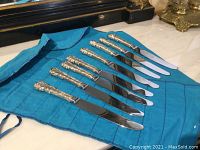 Seven knives laid out on blue fabric roll, showing handles and blades.