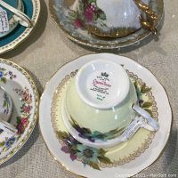 Six assorted porcelain cups and saucers showing backside markings with brand names and details.