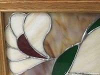 Close-up image showing cream-colored swirled glass with red accent and silvery lead lines in a floral or leaf design within a wooden frame.