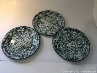 Photo showing three antique spatterware metal plates with green and white splatter pattern, arranged overlapping on a light surface.