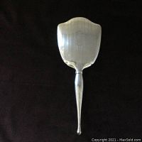 Sterling silver vanity hand mirror with smooth polished frame and handle, shield-shaped reflective surface.