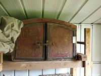 Front view of antique wooden cabinet showing double doors with iron latch and weathered wood with faded red paint.