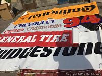 Photo showing four large automotive vinyl/plastic banners laid out primarily showing Continental, Chevrolet, General Tire, and Bridgestone brand names.