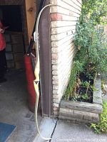 Full view of wooden recurve archery bow leaning against brick wall near garden bed showing black limb tips and natural wood finish