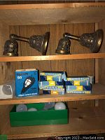 Two ornate brass wall sconces on wooden shelf with boxes of light bulbs below.