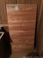 Photo showing full view of rectangular butcher block tabletop leaning against wall, displaying natural wood finish and visible wear.