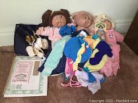 Three Cabbage Patch Kids dolls, doll clothes, a dark tote bag, and paper documents.