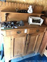 Front view of the wood cabinet showing two drawers with metal handles and two cupboard doors below. Shelf and scalloped backboard at top visible. Worn wood surface.