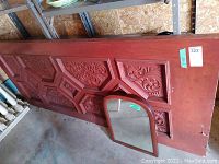 Photo of large reddish-brown wood carved door lying on the floor in a garage area with detailed carvings in panels.