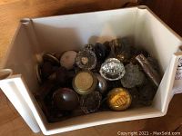 Wide view of white plastic bin filled with assorted vintage door knobs made of glass, brass, wood, porcelain, and metal showing wear and patina.