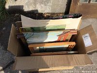 Top view of a box containing assorted framed prints with wooden and one metal frame.