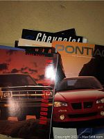 Colorful GM car brochures including Chevrolet Suburban and Pontiac models visible