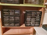 Three black plastic storage drawers units filled with assorted nuts, bolts, screws, washers, and hardware items on wooden shelving.